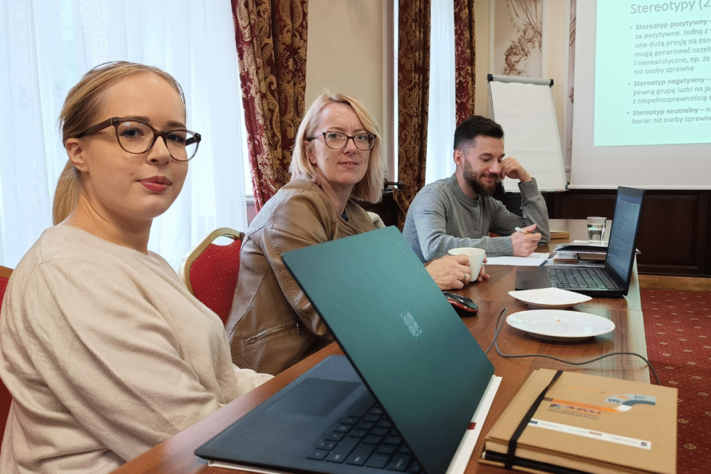 zdjecie przedstawia 3 osoby siedzace przy stole sali szkoleniowej i uczestniczące w szkoleniu