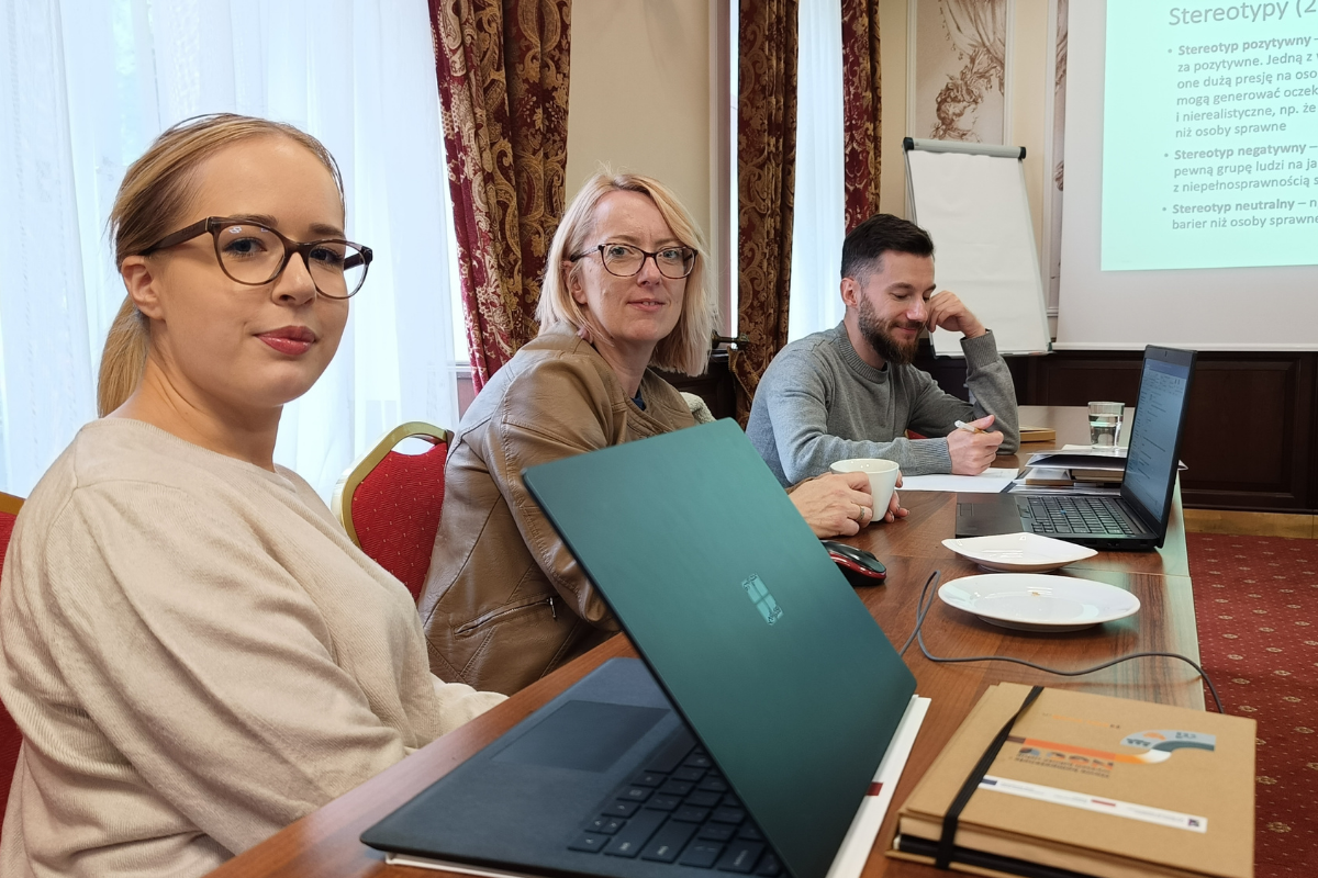 zdjecie przedstawia 3 osoby siedzace przy stole sali szkoleniowej i uczestniczące w szkoleniu