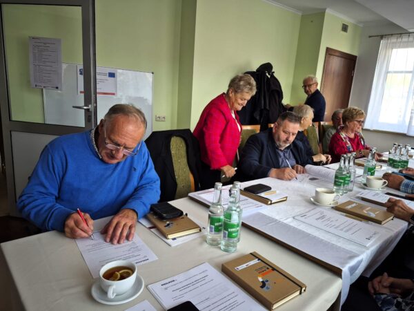 zdjecie przedstawia osoby siedzace przy stole sali szkoleniowej i uczestniczące w szkoleniu