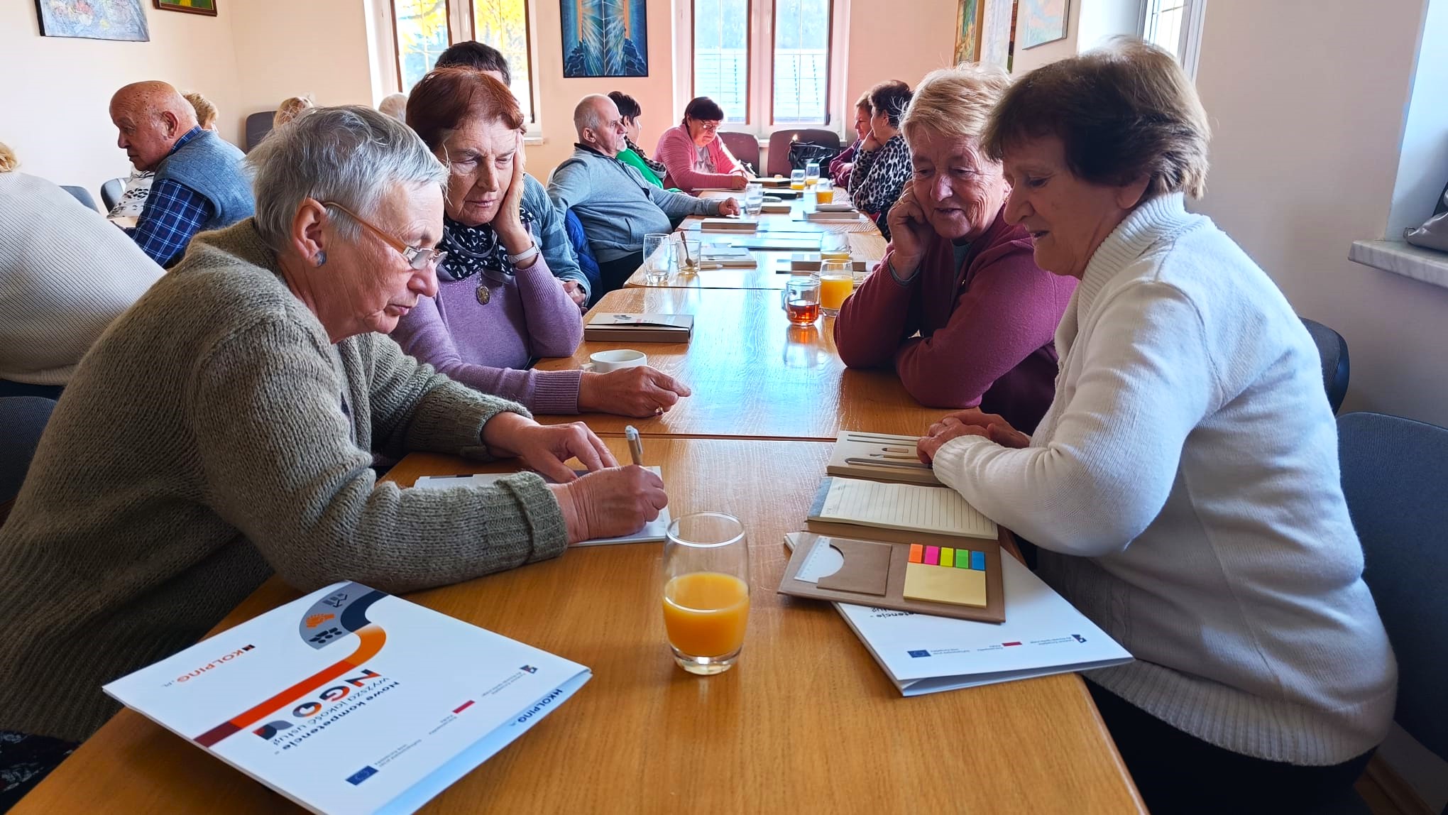 zdjecie przedstawia osoby siedzace przy stole sali szkoleniowej i uczestniczące w szkoleniu