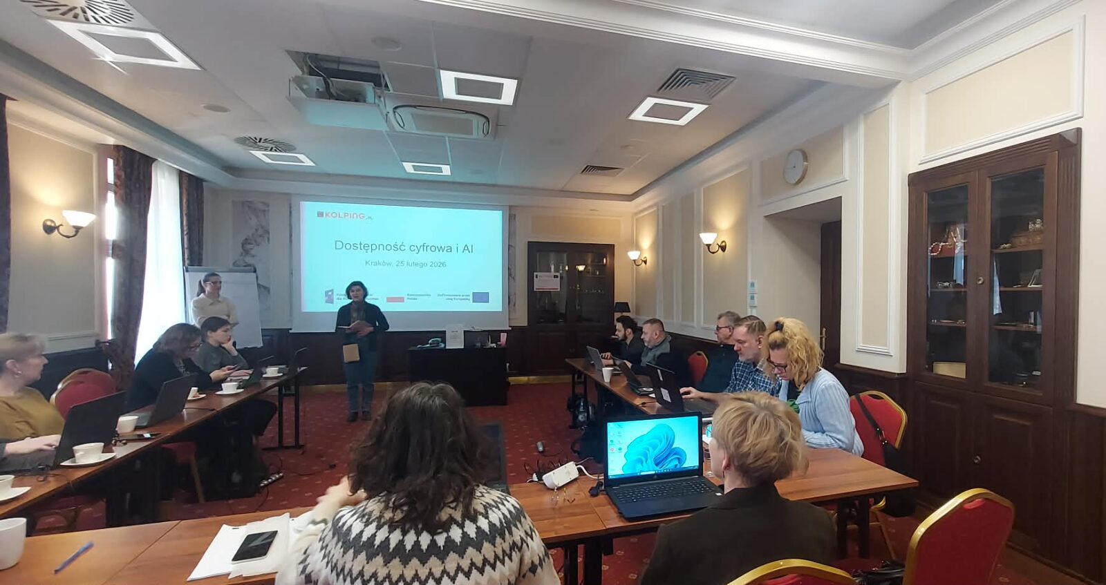 zdjęcie przedstawia uczestników szkolenia siedzących przy stołach, w tle ekran z prezentacją